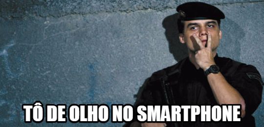 Foto do personagem Capitão Nascimento, interpretado por Wagner Moura no filme Tropa de Elite, de farda policial com a mão próxima ao rosto apontando os dedos indicador e médio aos seus olhos, com o texto "tô de olho no smartphone" na parte inferior da imagem.