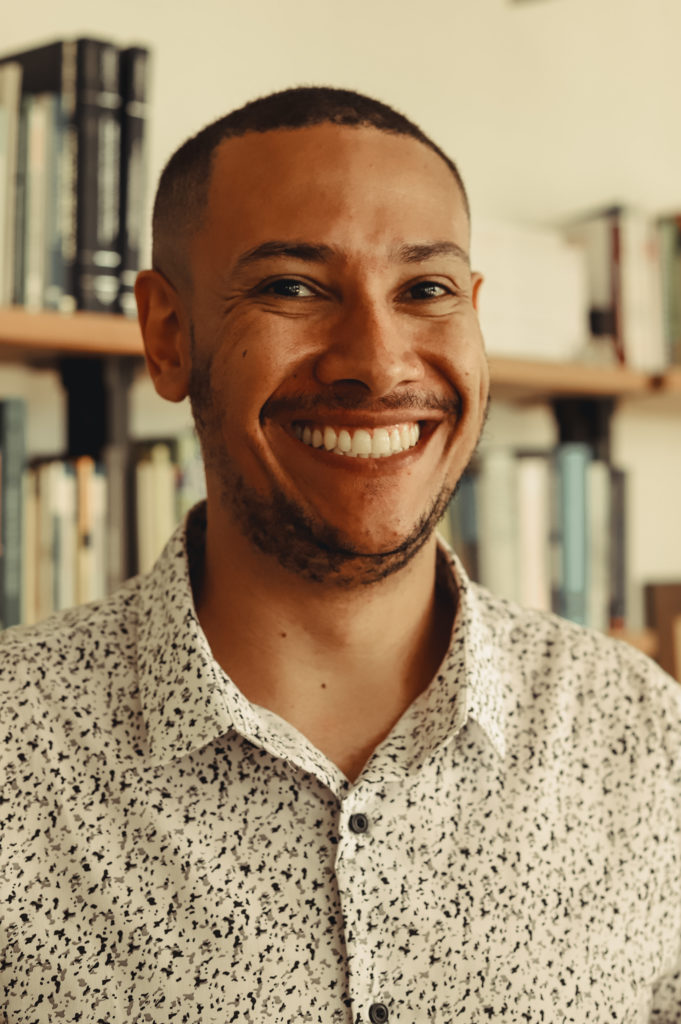 Foto de Luiz Fernando Sabino, homem negro, de barba e cabelos curtos. Ele veste blusa branca com detalhes pretos e botões na frente. e está sorrindo. Créditos para Bianca Moreira/InternetLab.